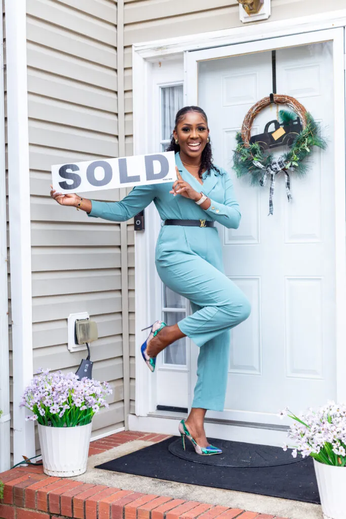 Ama holding a SOLD sign on a home's front porch