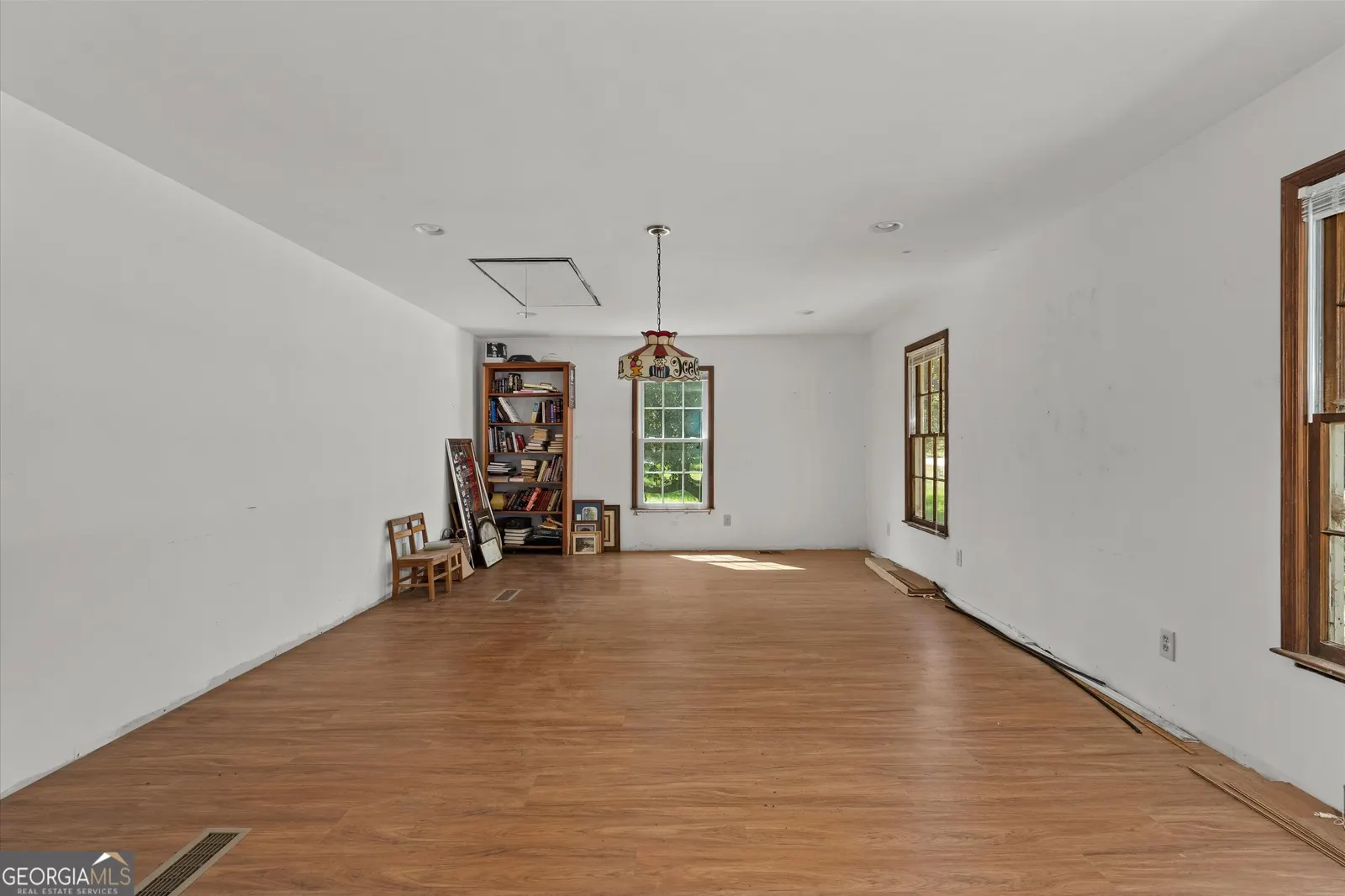 Long open room with hardwood floors and a hanging lantern, empty apart from shelving at the far end
