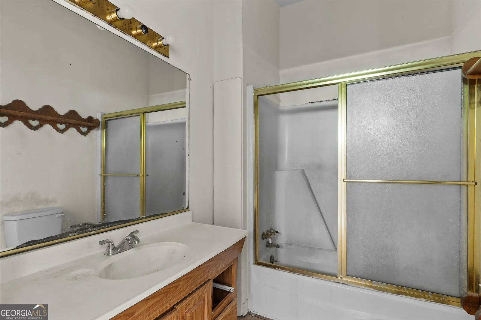 Bathroom with a wood vanity, a wide mirror and a gold-framed sliding shower door over the tub
