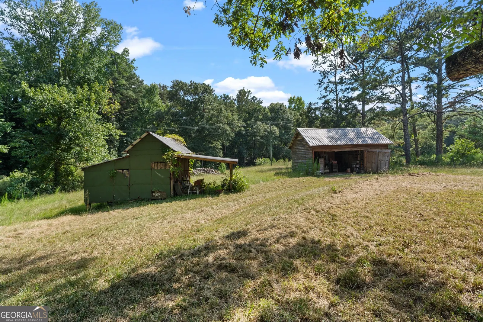 Two outbuildings, a green shed and an open equipment shelter, in a clearing backed by woods