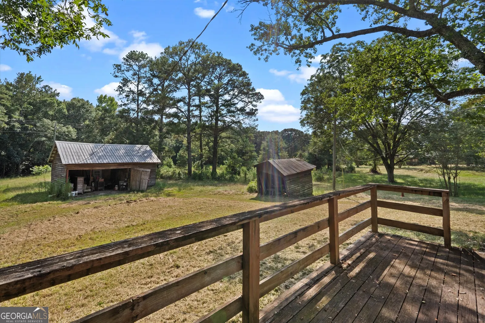 A barn and a small outbuilding on open grass, with pines behind