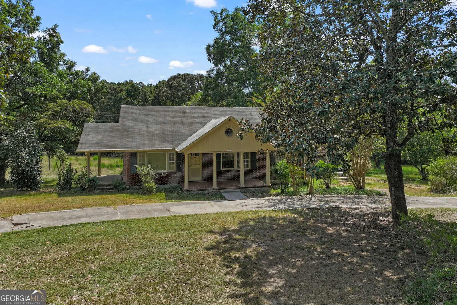 The house from the driveway, with crepe myrtles along the front and mature trees behind