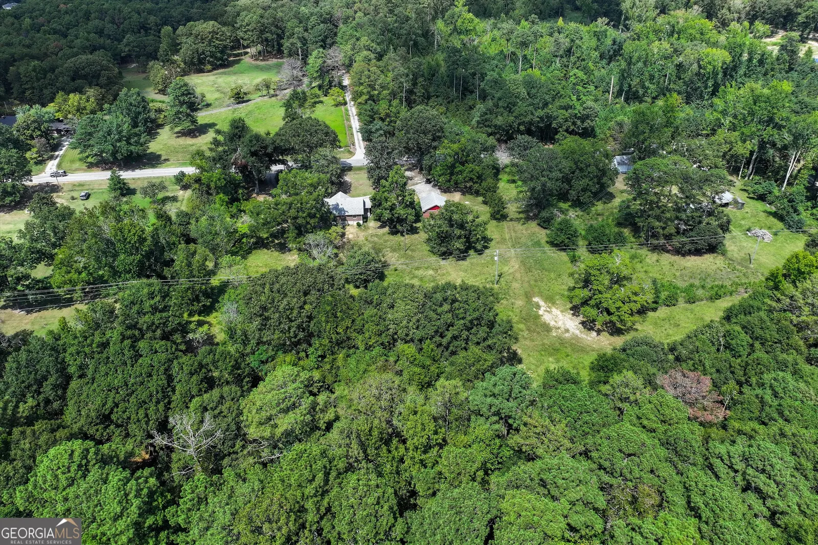 Aerial showing the open lawn and driveway within the wooded parcel