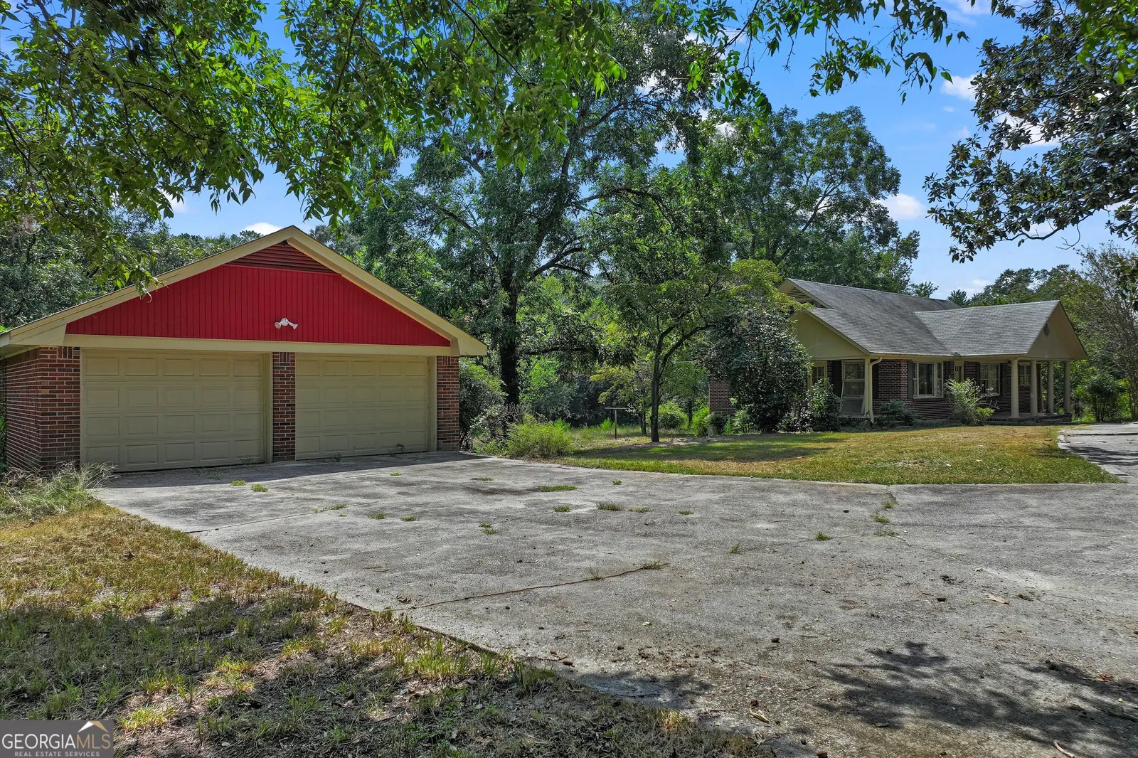 Detached garage with a red gable end and two bays, across a wide concrete apron from the house