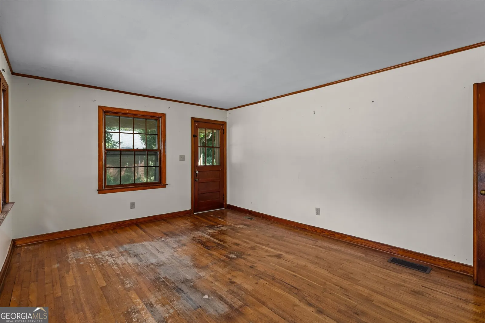 Empty room with hardwood floors, wood-trimmed windows and a panelled door