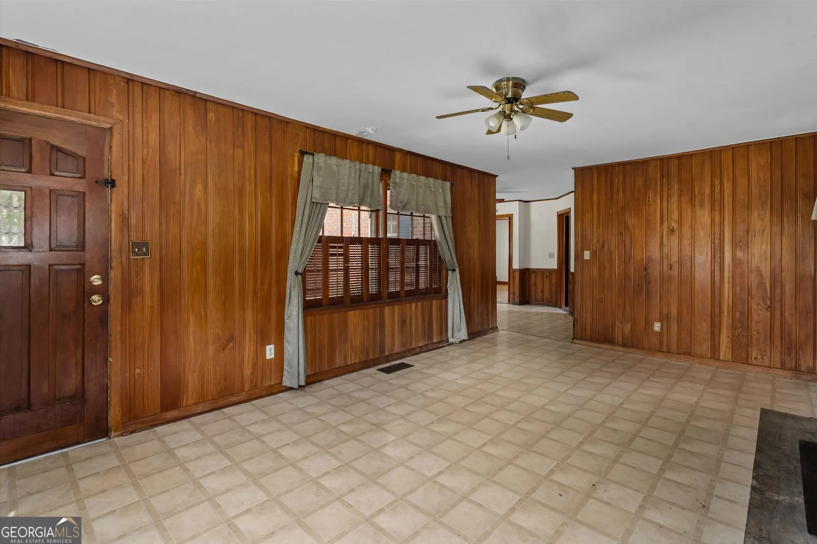 Panelled room with the front door, a ceiling fan and tile flooring