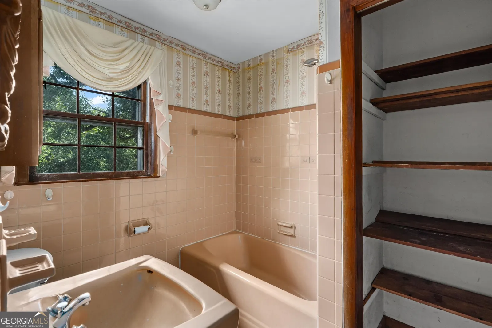 Bathroom with pink tile, a built-in linen shelf and a window above the tub