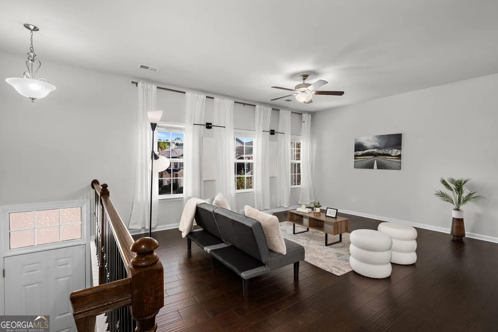 Living room with dark hardwood floors, a ceiling fan and a row of tall front windows, staged with a sofa and coffee table