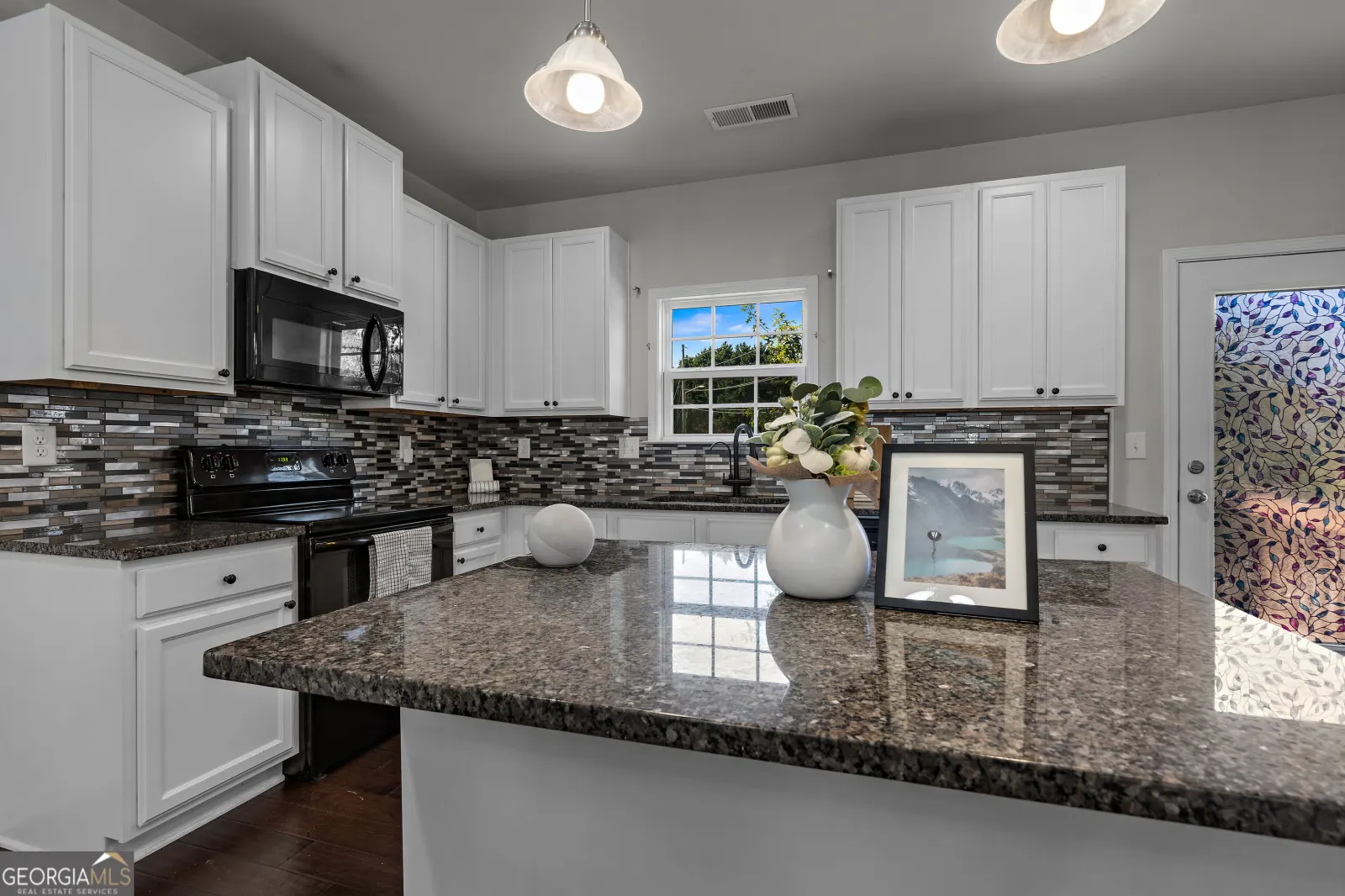 Kitchen island with a dark stone countertop, white cabinets and a mosaic tile backsplash