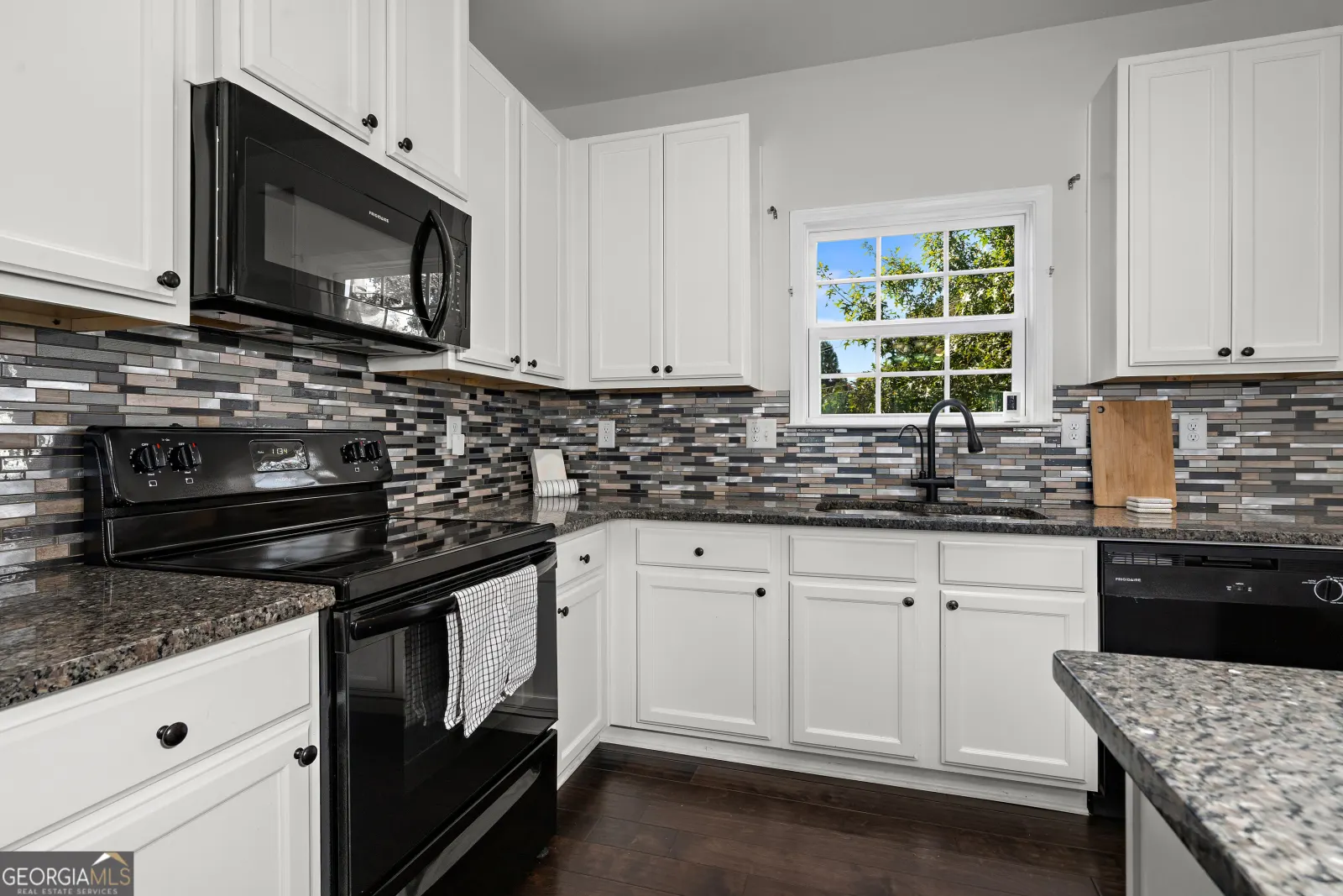 Kitchen with white cabinets, black appliances and a window over the sink