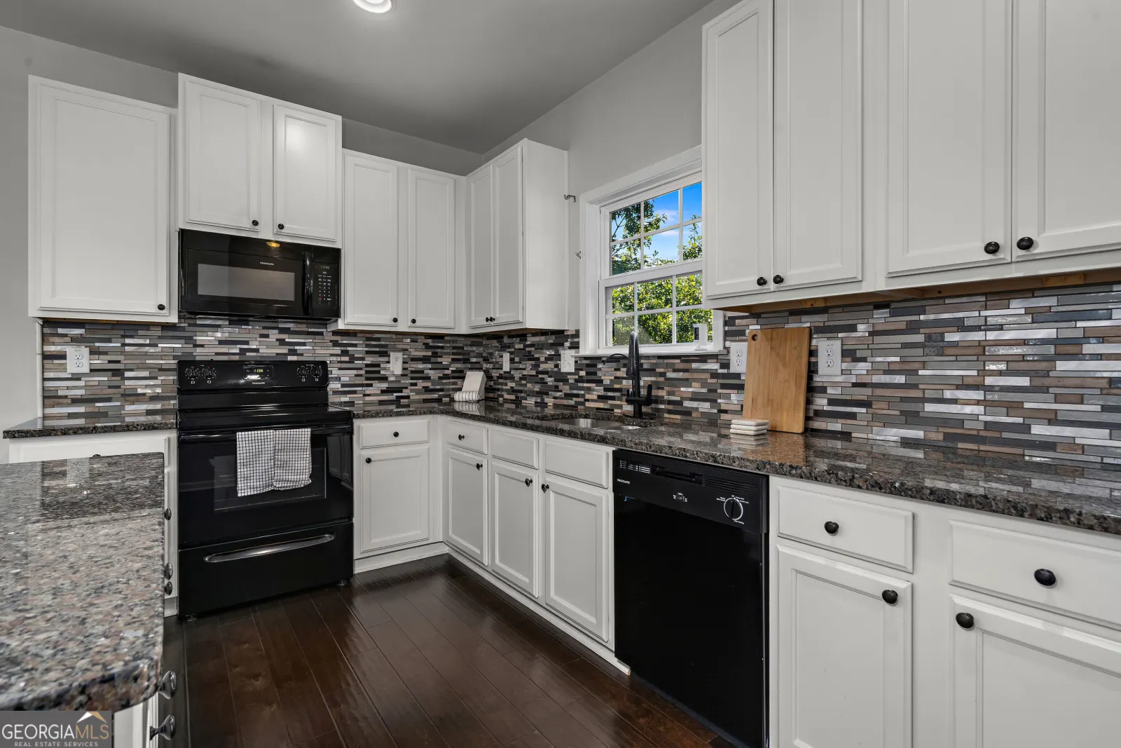 Kitchen counter run with a black range, microwave and dishwasher under white cabinets