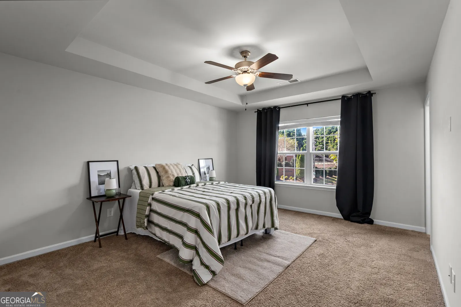 Primary bedroom with a tray ceiling, ceiling fan and carpet
