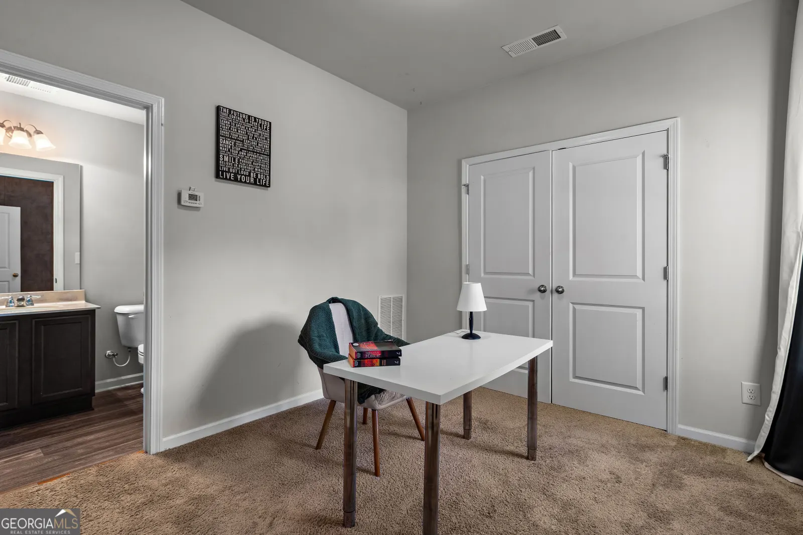 Entry-level bedroom staged with a desk, with double closet doors and its bathroom beyond