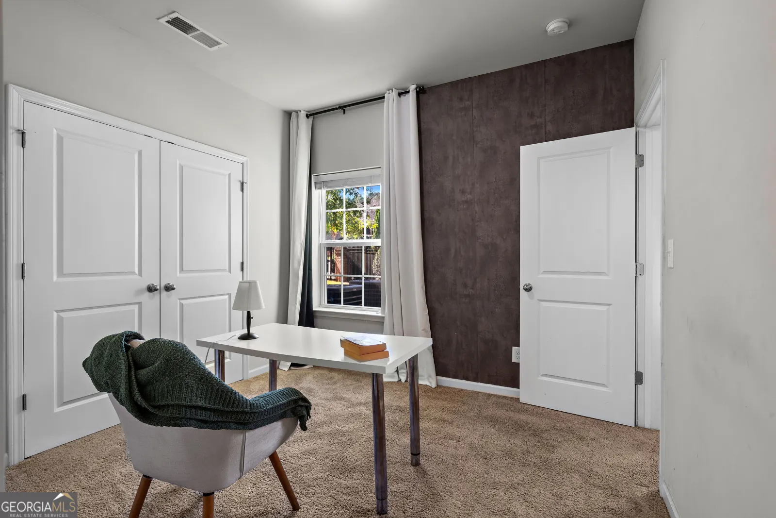 Entry-level bedroom with double closet doors and a window, staged with a desk